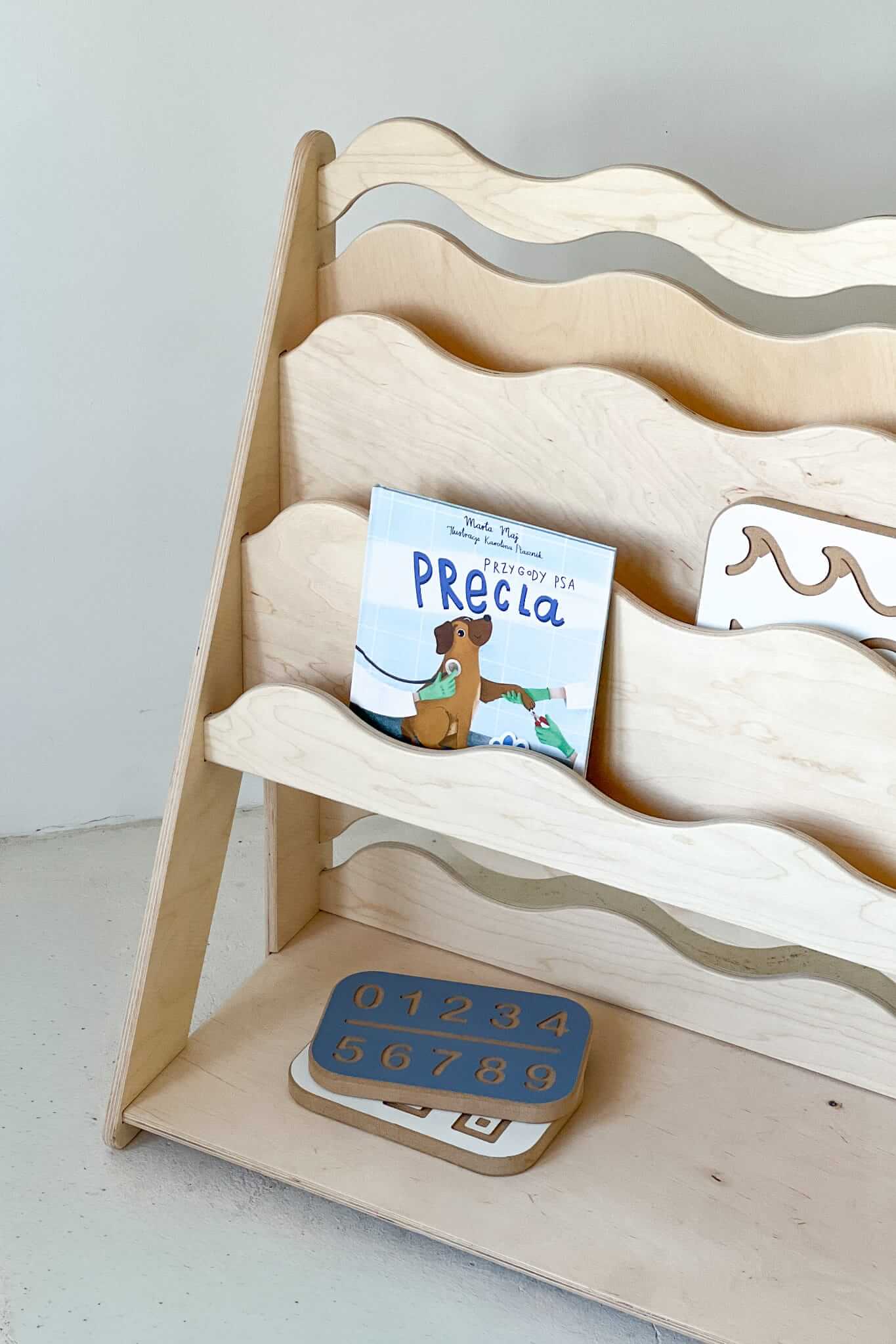 Bücher- und Spielzeugregal "WAVE" aus Holz, versch. Größen mit einem Buch und Zahlenpuzzle.