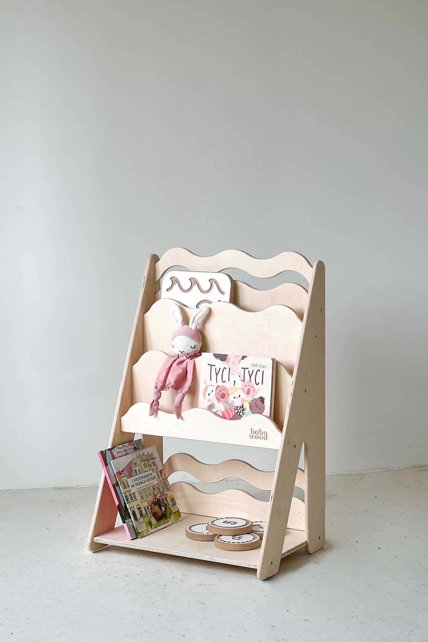 Bücher- und Spielzeugregal "WAVE" aus Holz, versch. Größen mit bunten Büchern und einem Stofftier.