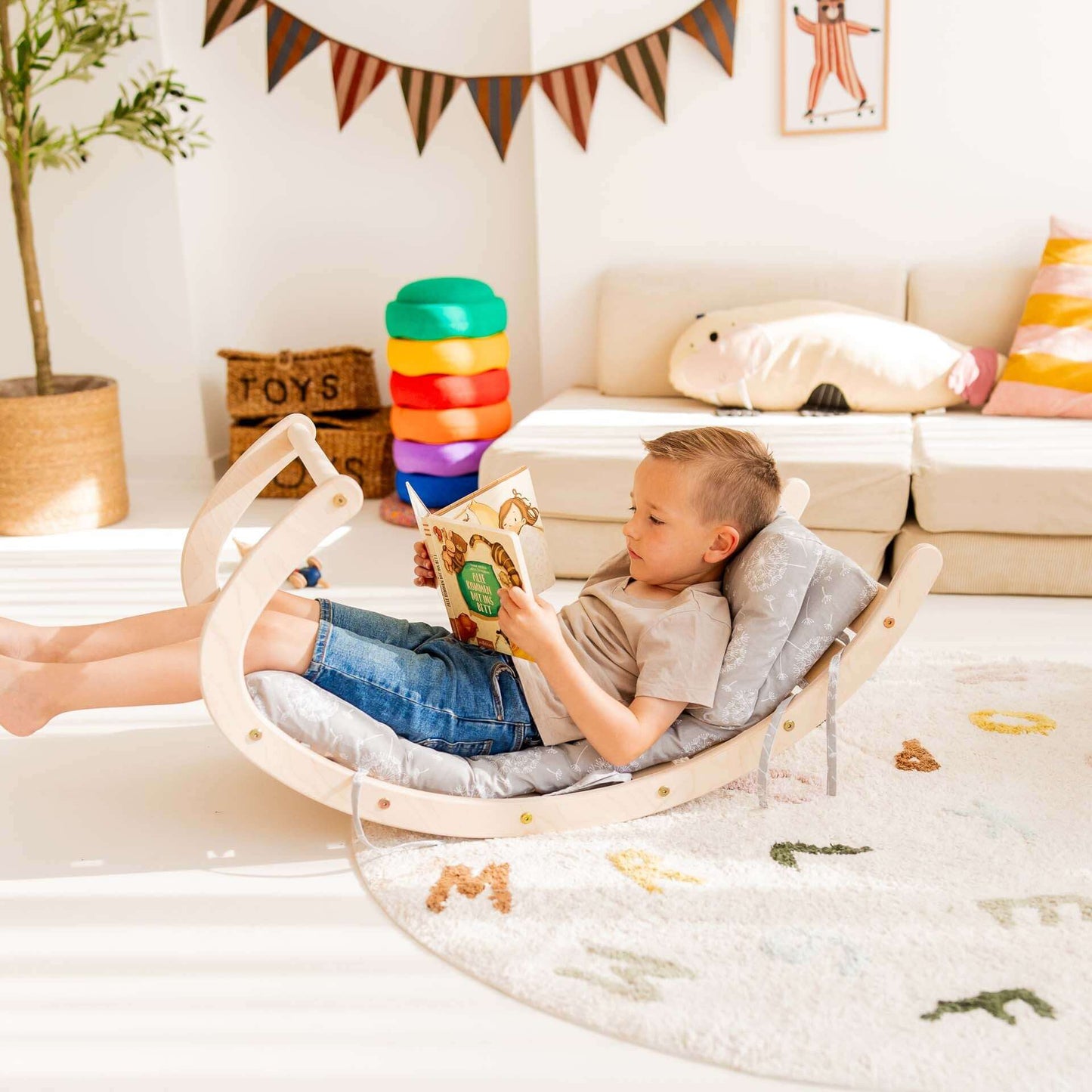 Junge liest in einer Kletterbogen Äffchen Wippe aus Holz im hellen Spielzimmer.