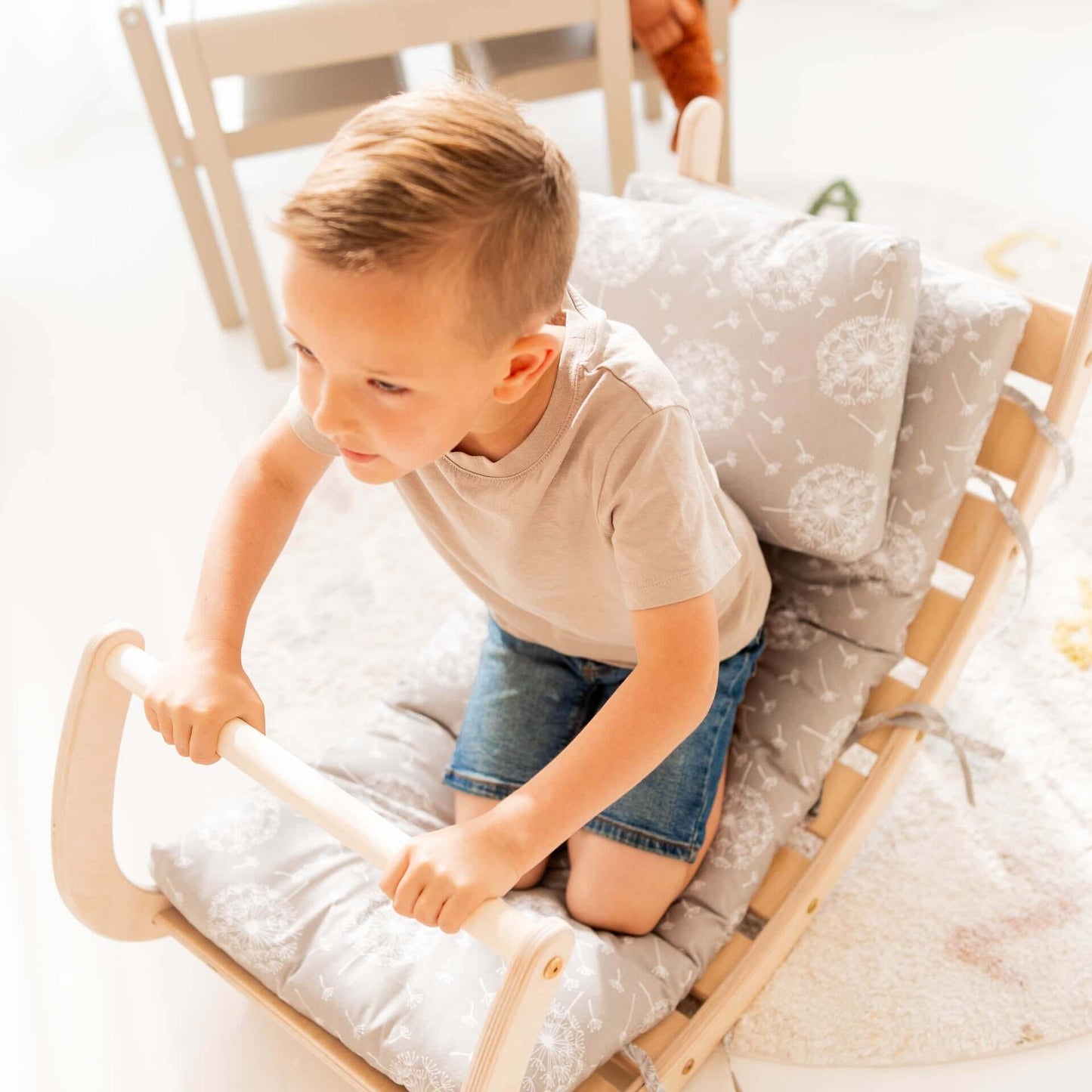 Kleiner Junge, der auf einem Kletterset Äffchen mit Kissen sitzt und sich an der Holzstange festhält.