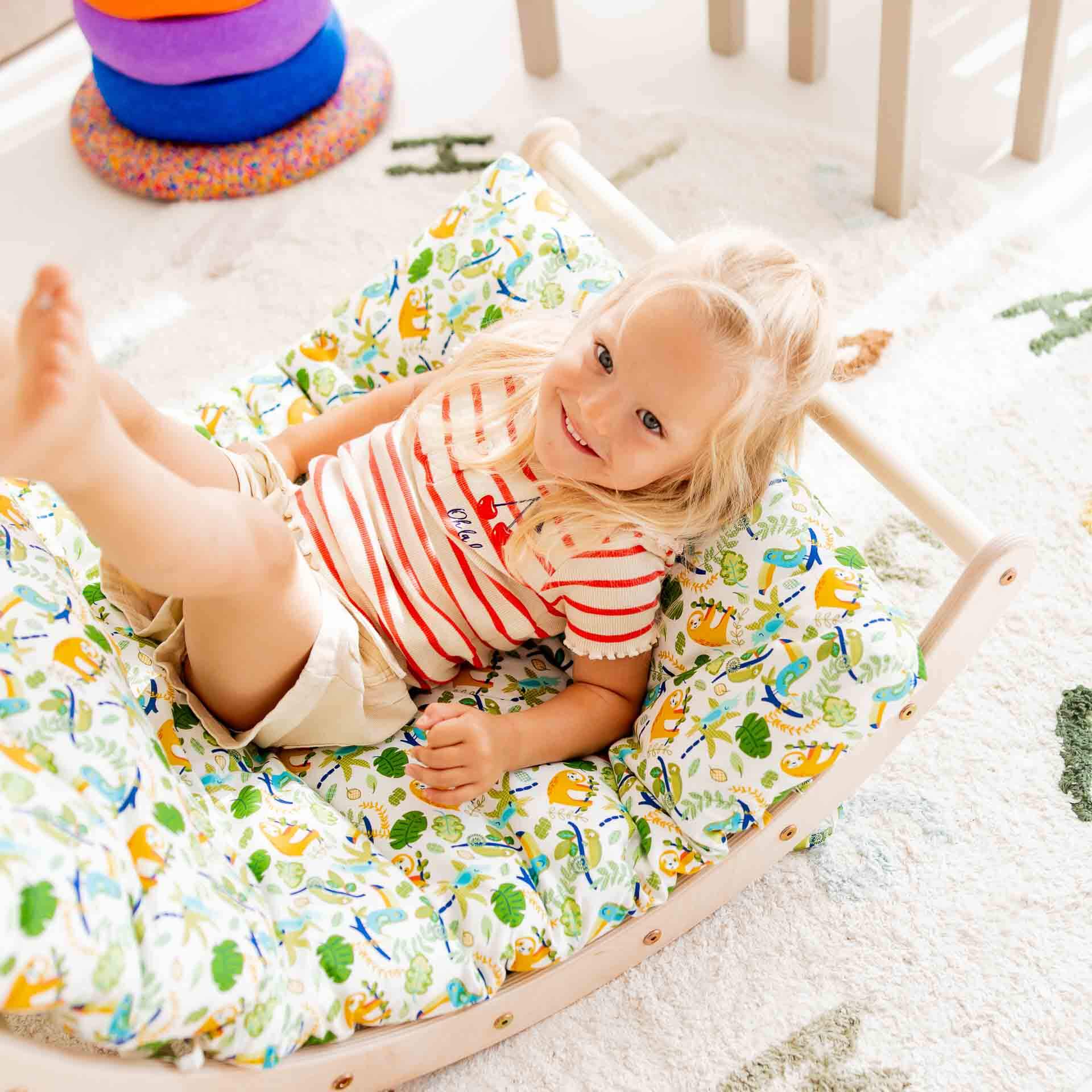 Glückliches Kind spielt auf dem Kletterbogen Basic, umgeben von bunten Kissen und Spielzeug.