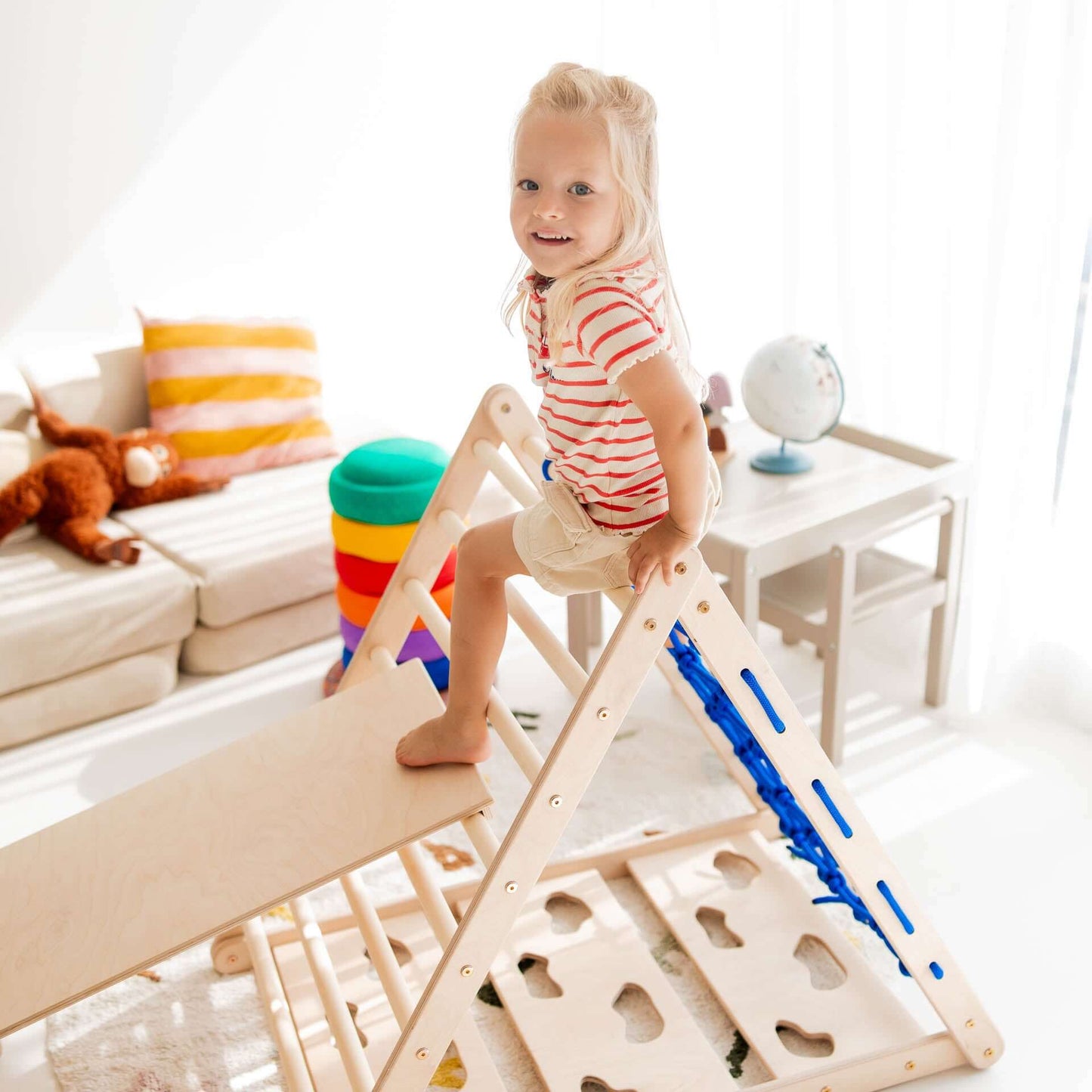 Ein glückliches Kind spielt auf dem Kletterdreieck Äffchen aus Holz mit Rutsche und Schaukel in einem hellen Spielzimmer.