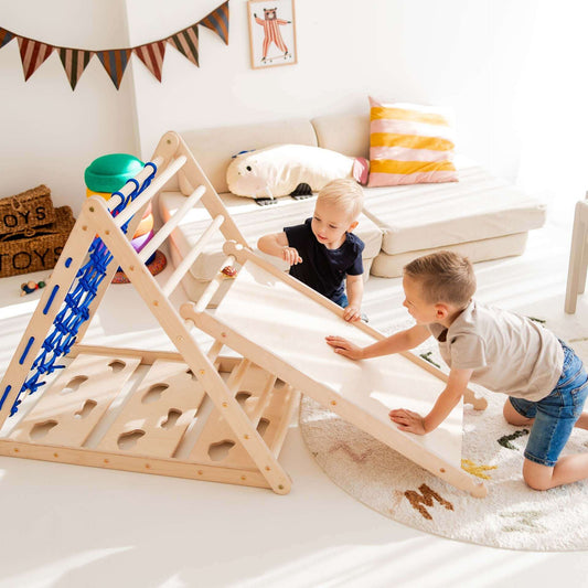 Zwei Kinder spielen mit einem Rutschbrett / Hühnerleiter, das mit einem Kletterdreieck kombiniert ist.
