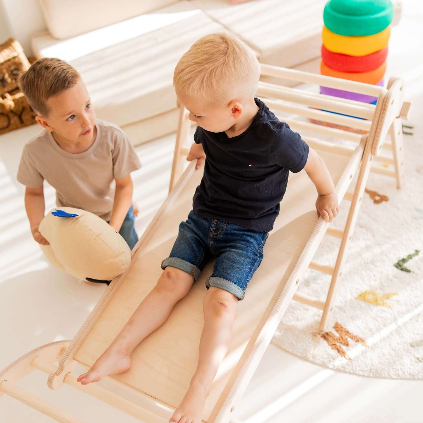 Zwei Kinder spielen mit dem Kletterset Panda, einer Rutsche und einem Kletterdreieck in lebhaftem Spielzimmer.