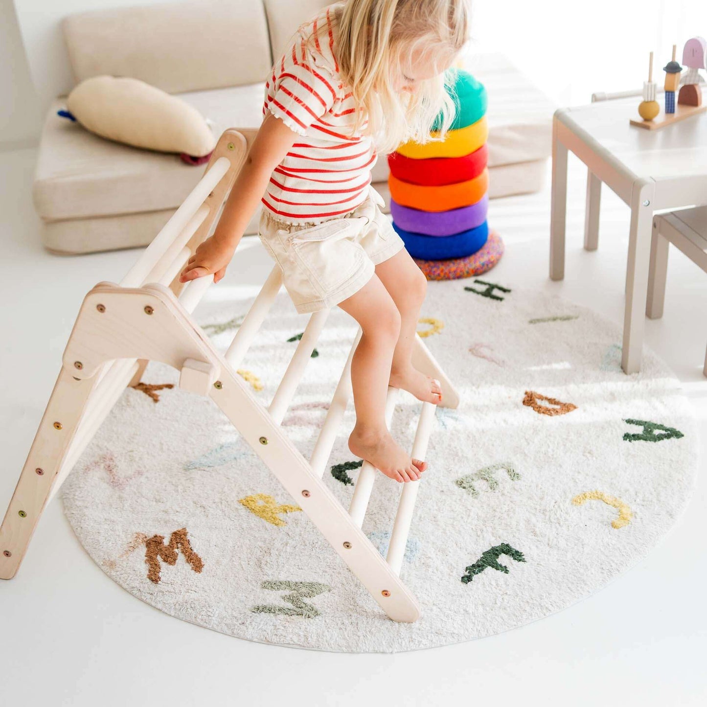 Kind spielt auf dem faltbaren Kletterdreieck Lina aus Holz auf einem bunten Teppich.