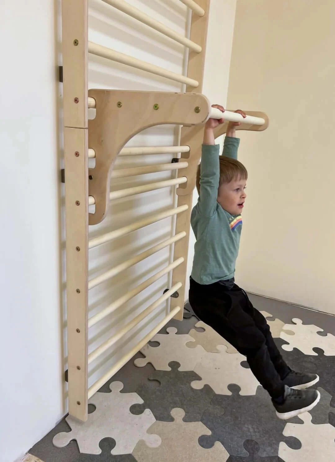 Kletterwand für Kinder aus Holz, Kleinkind übt Klimmzüge an Sprossenwand im Spielzimmer.