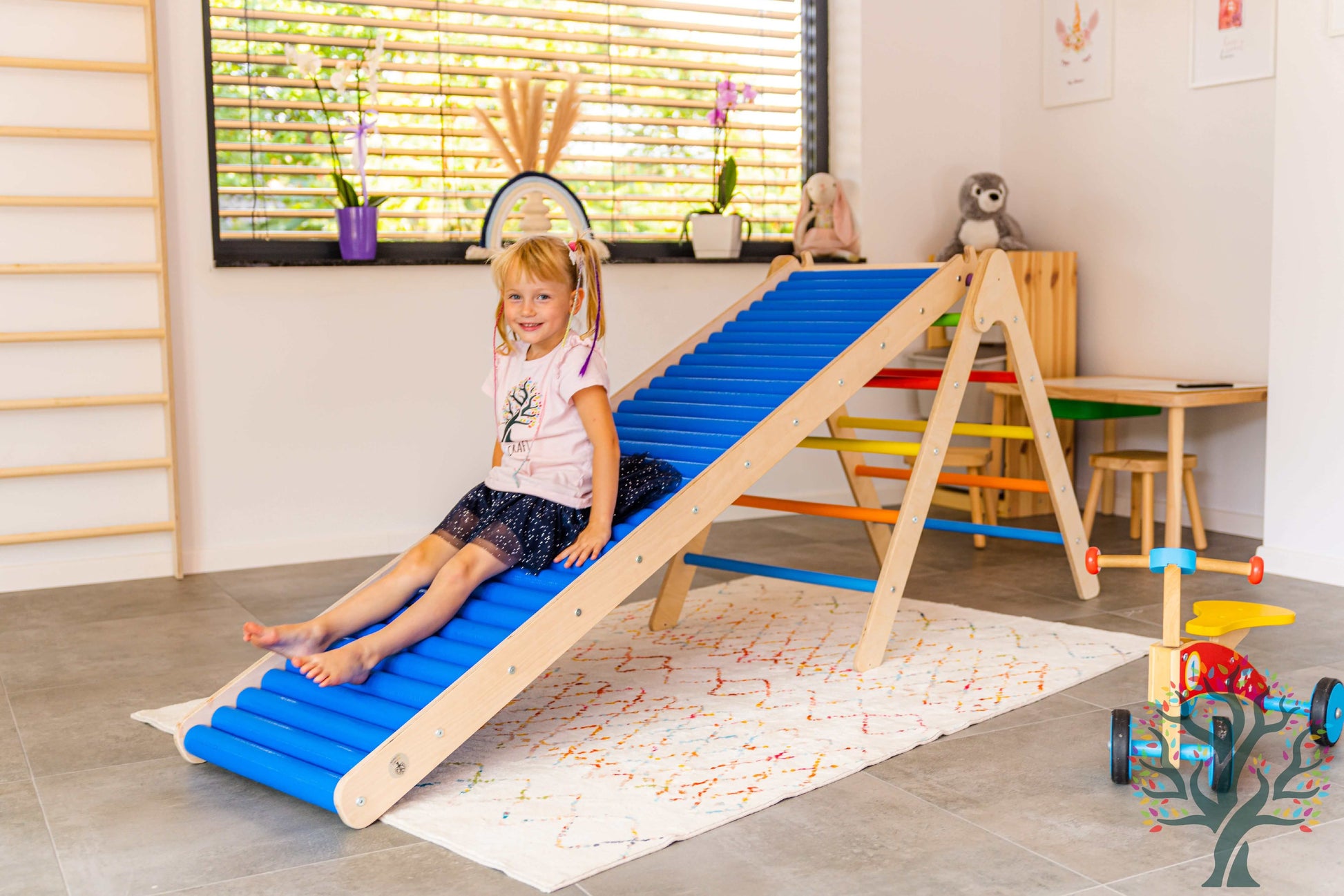 Mädchen spielt mit der Rollenrutsche für Kinder, versch. Größen, in einem hellen Raum mit Holzspielzeug.