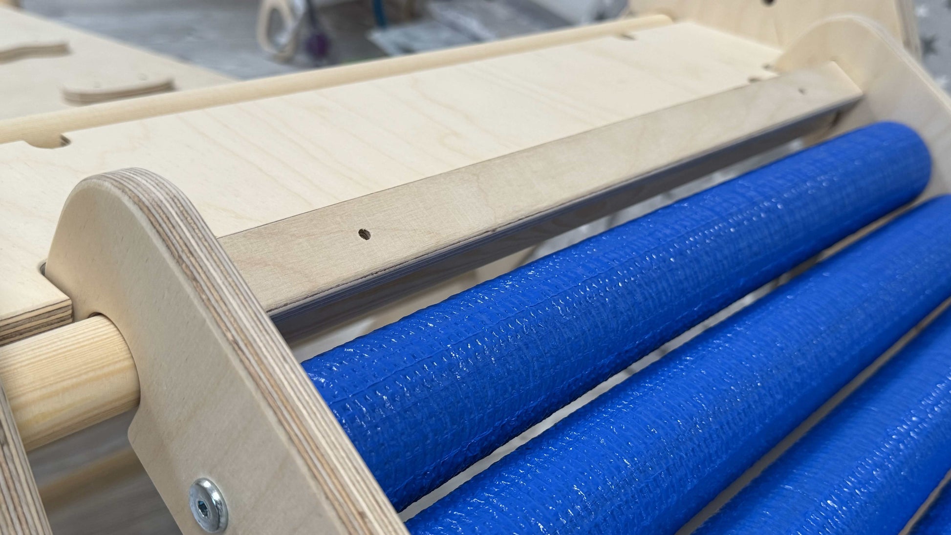 Detailansicht der Rollenrutsche für Kinder, versch. Größen mit blauen Schaumstoffrollen und Holzrahmen.