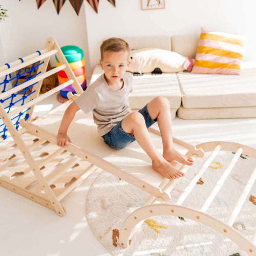 Junge rutscht auf Kletterset Löwe, bestehend aus Kletterdreieck und Kletterbogen, aus Holz, in einem sonnigen Raum.